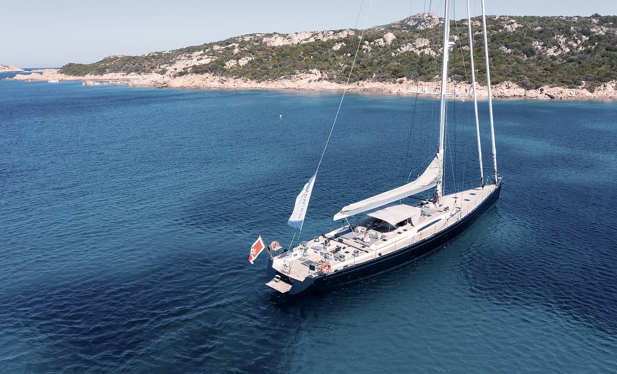 Sailing Yacht Freebird at anchor in clear water below a rocky shoreline