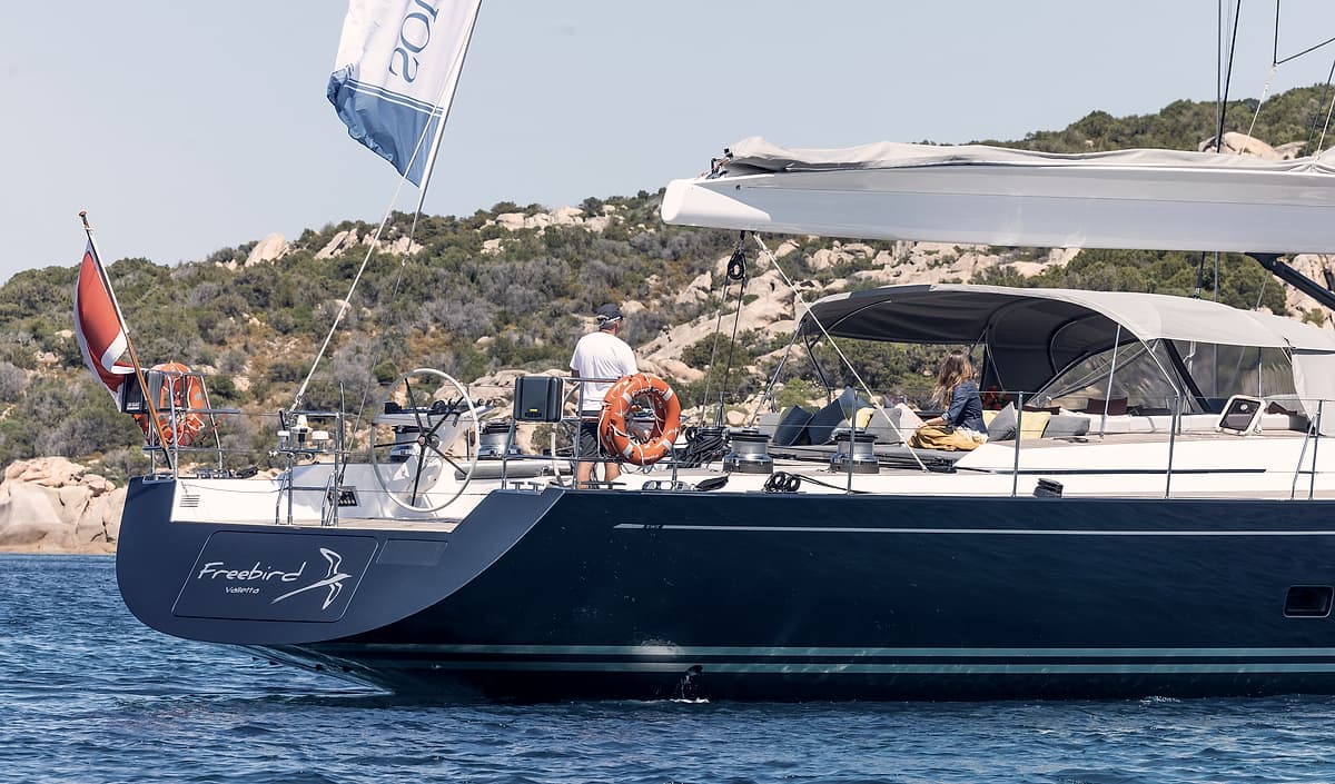 The hull and cockpit of Sailing Yacht Freebird at anchor off a rocky shore